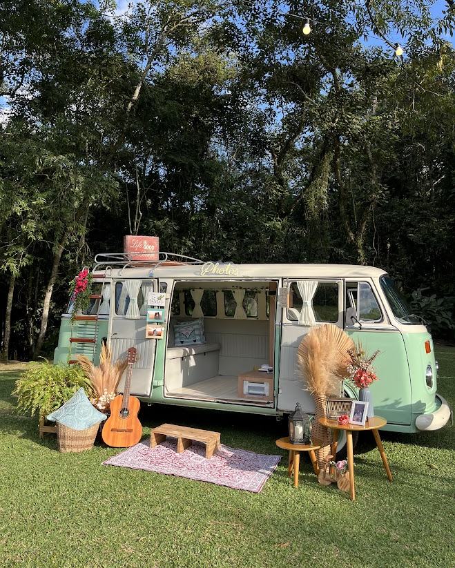 Kombi retrô da La Kombine montada no gramado, com violão, tapete e luzes, pronta para receber os convidados