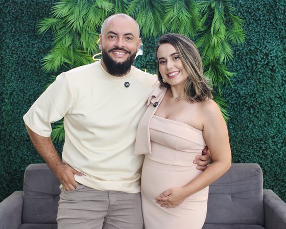 Casal posando para o totem fotográfico em frente ao painel de folhagem